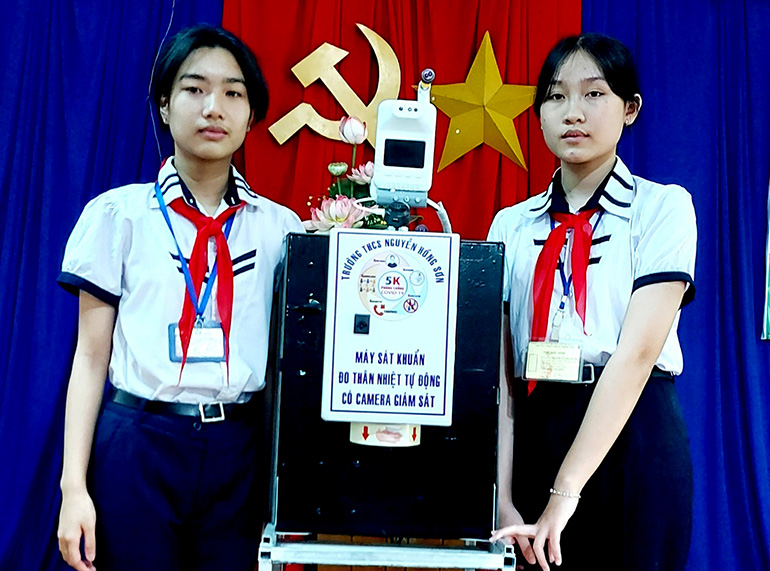 Hai em Trần Mai Phương Quỳnh và Nguyễn Lê Quỳnh Mai bên Máy sát khuẩn, đo thân nhiệt tự động có camera giám sát. Ảnh: KHẮC QUÂN